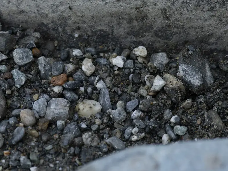 Small grey and white pebbles of different sizes lie packed between two larger smooth stones.