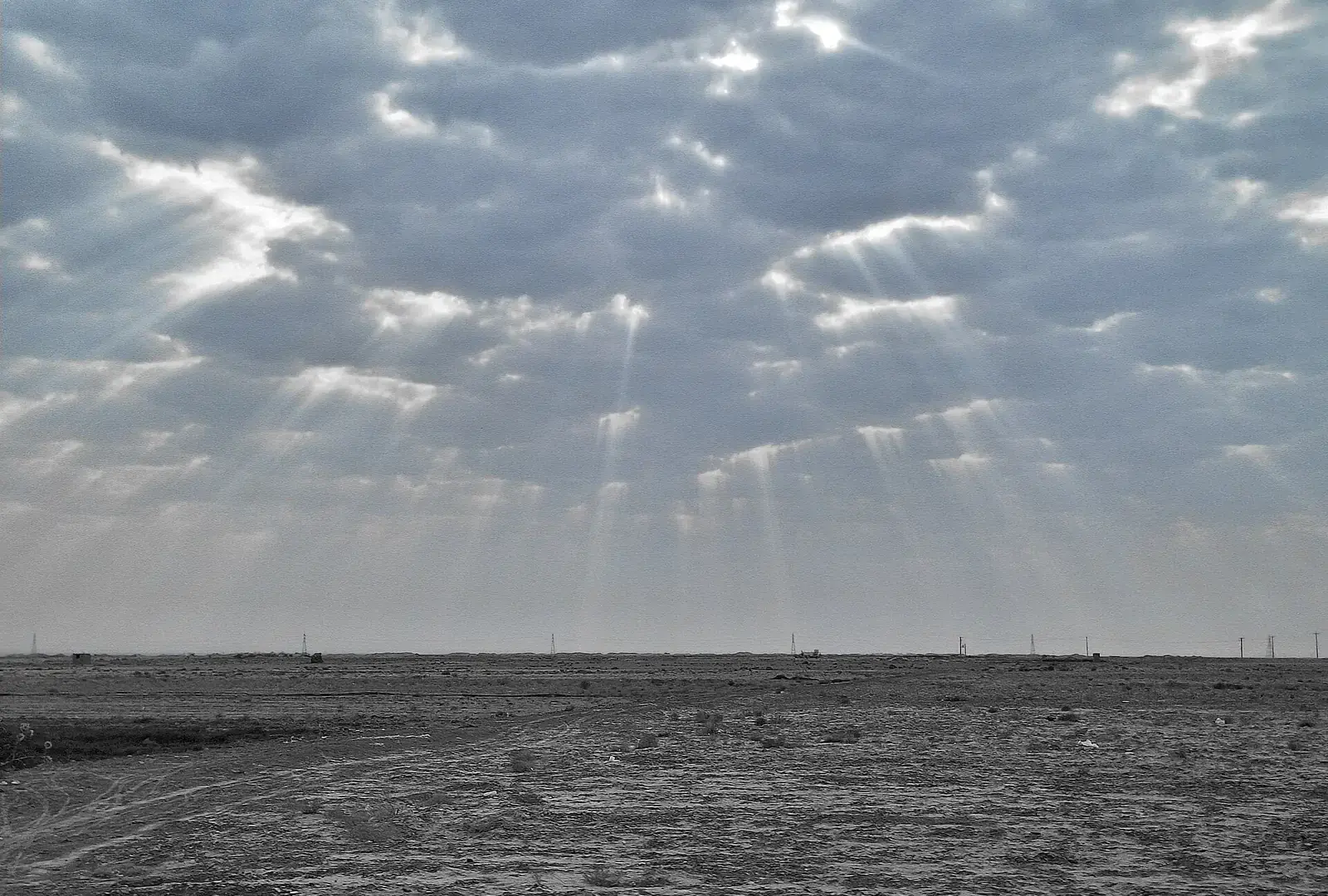 A wide sky of broken cloud with light breaking through, over flat open ground.