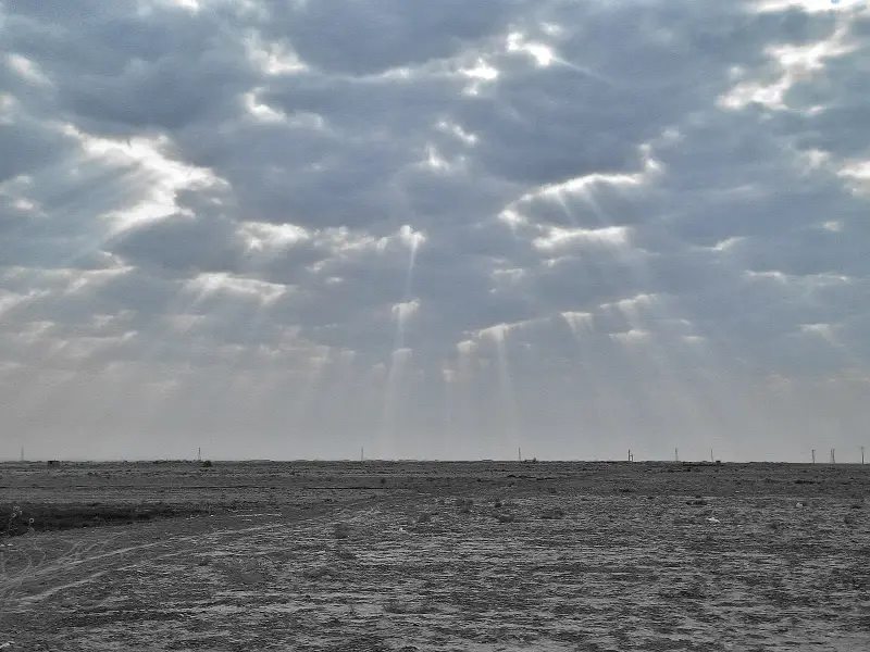 A wide sky of broken cloud with light breaking through, over flat open ground.